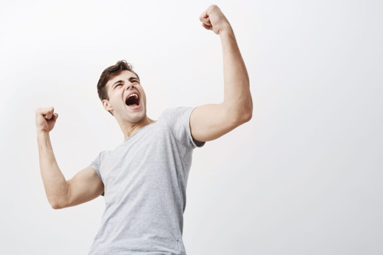 Close up of successful young caucasian male sportsman screaming Yes and raising clenched fists in the air, feeling excited. People, success, triumph, victory, winning and celebration